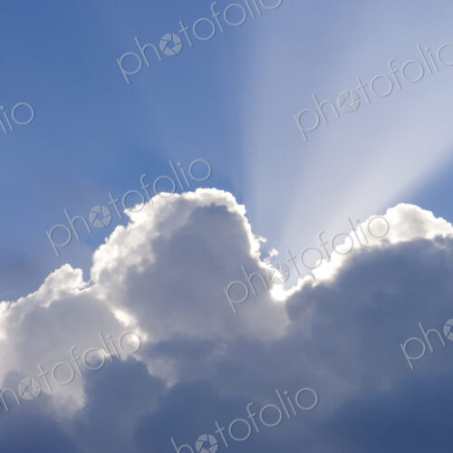 Sun shining behind cumulonimbus clouds in a blue sky. Sun shining behind cumulonimbus clouds in a blue sky.