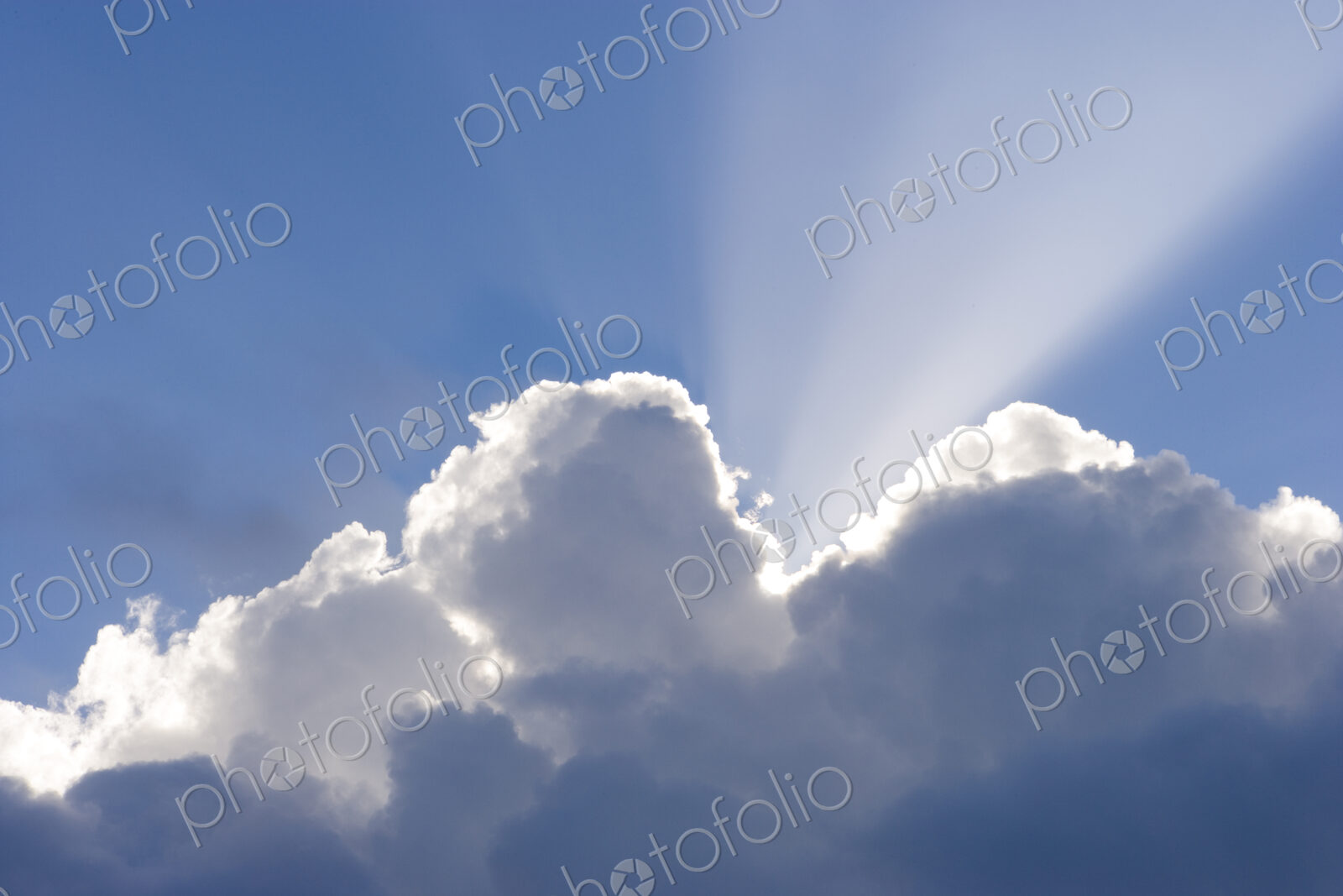 Sun shining behind cumulonimbus clouds in a blue sky.