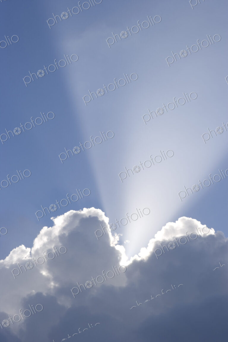 Sun shining behind cumulonimbus clouds in a blue sky.