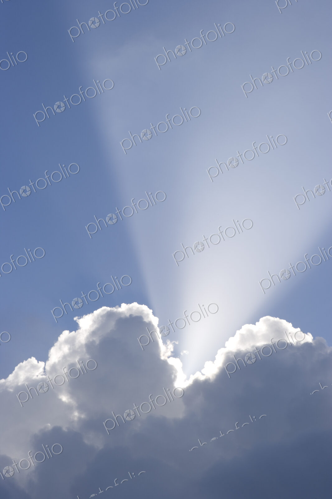 Sun shining behind cumulonimbus clouds in a blue sky.