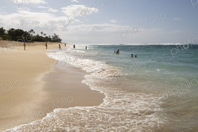 Sunbathers on Waimea Bay Beach on shore and in the water.