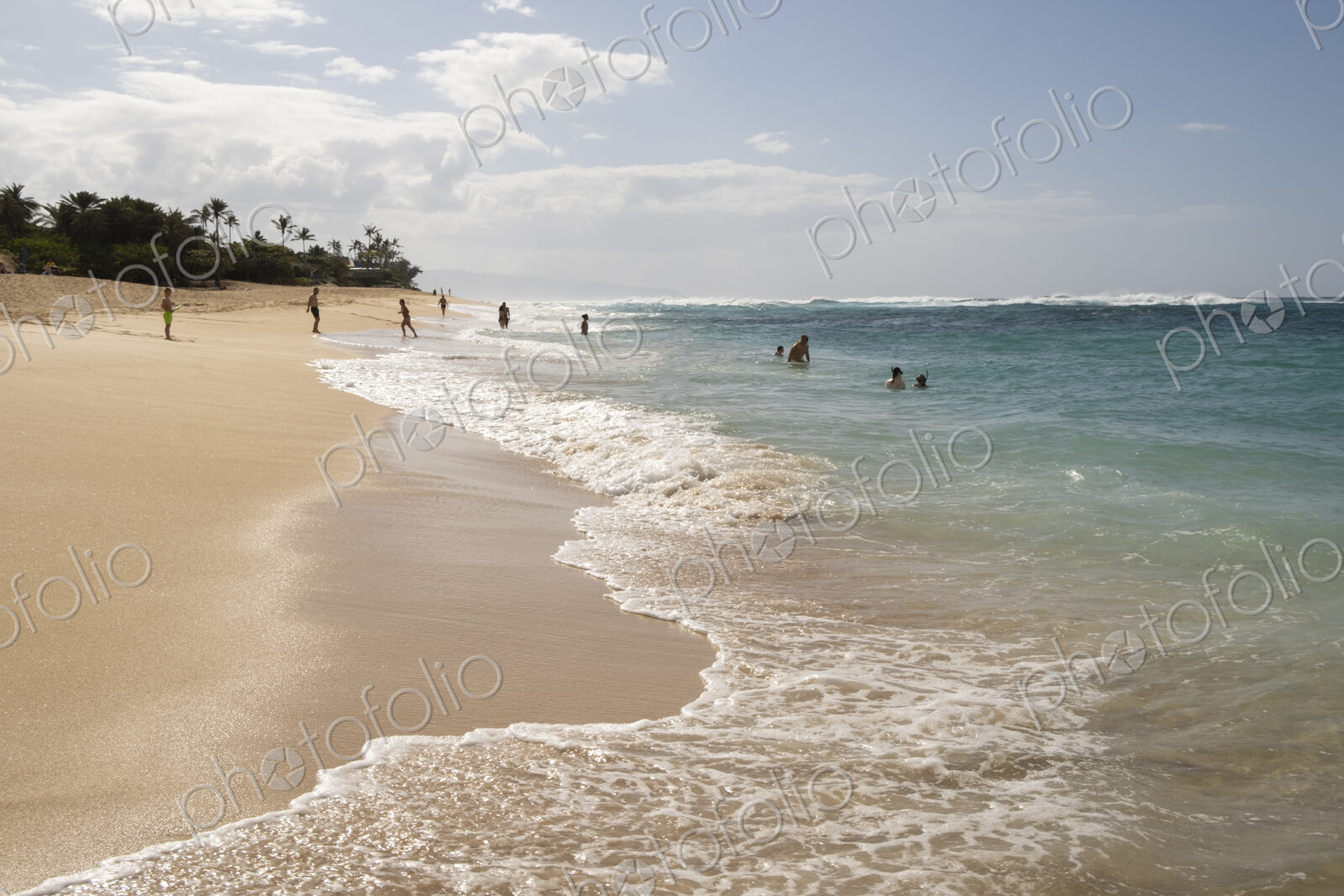 Sunbathers on Waimea Bay Beach on shore and in the water.