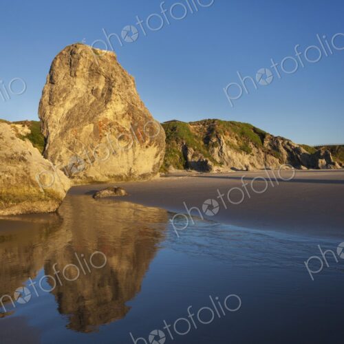 Sunlit rock formations reflect in the wet sand at low tide along the Oregon Coast in… Sunlit rock formations reflect in the wet sand at low tide along the Oregon Coast in…