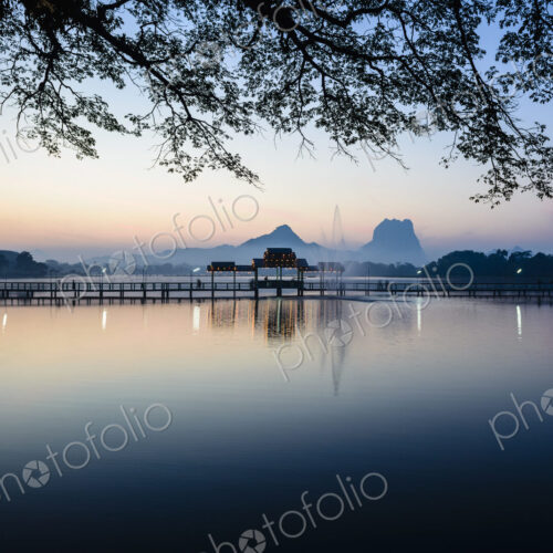Sunrise across a calm lake, a footbridge and pavilion, mountains in the distance. Sunrise across a calm lake, a footbridge and pavilion, mountains in the distance.