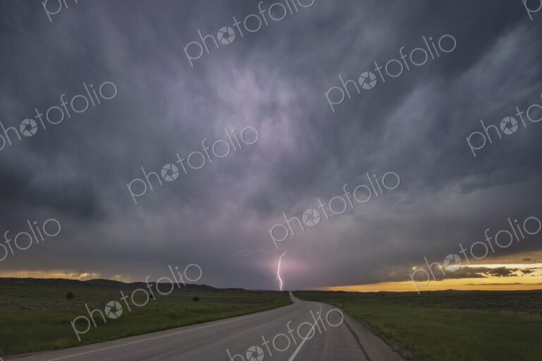 Sunset on WY Highway 59, view of the road ahead with cloud to ground lightning and…