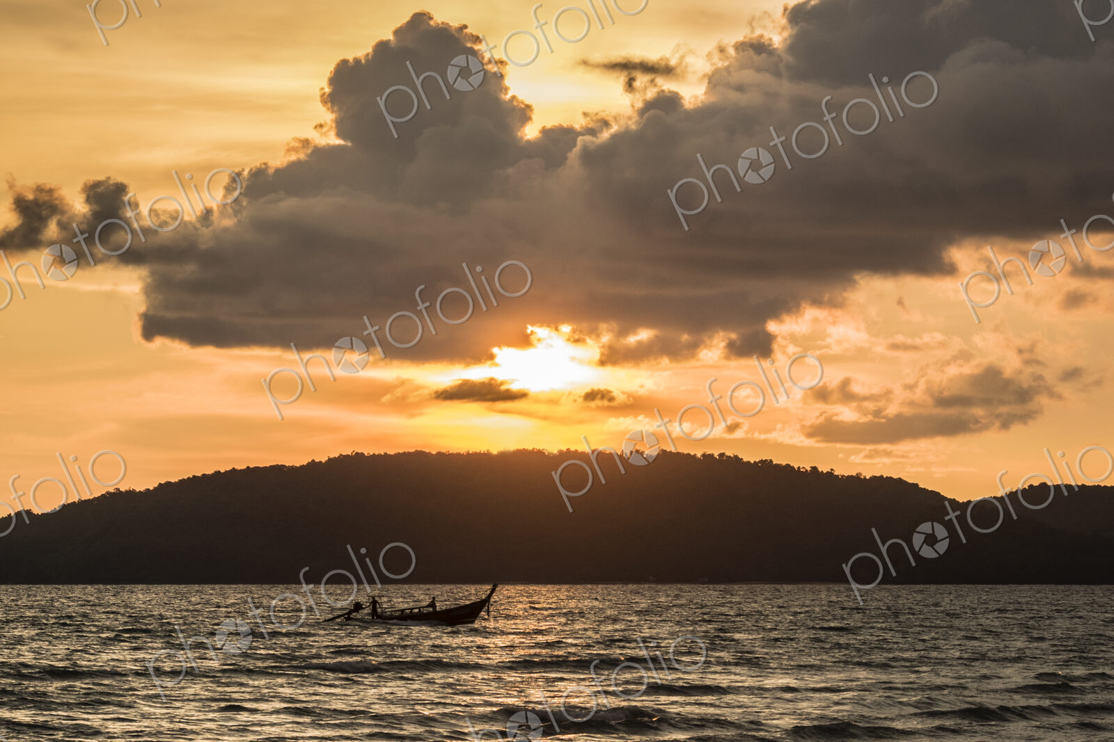 Sunset over wooded land with ocean in foreground.