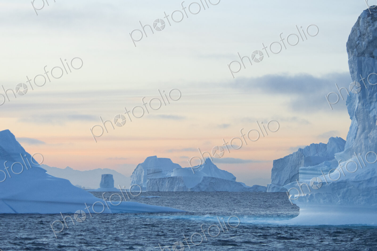 Sunset sky and floating icebergs with smooth eroded shapes on the waters of…