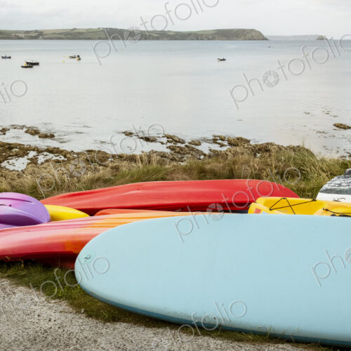 Surf boards and bodyboard, a kayak and boats on the sand on a beach, and view of the…