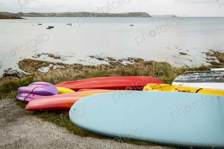 Surf boards and bodyboard, a kayak and boats on the sand on a beach, and view of the…