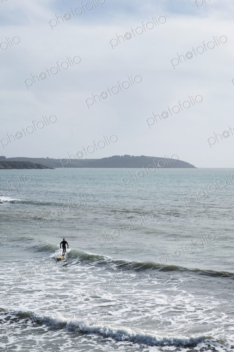 Surfer wearing wet suit riding ocean wave close to shore. need model release form!