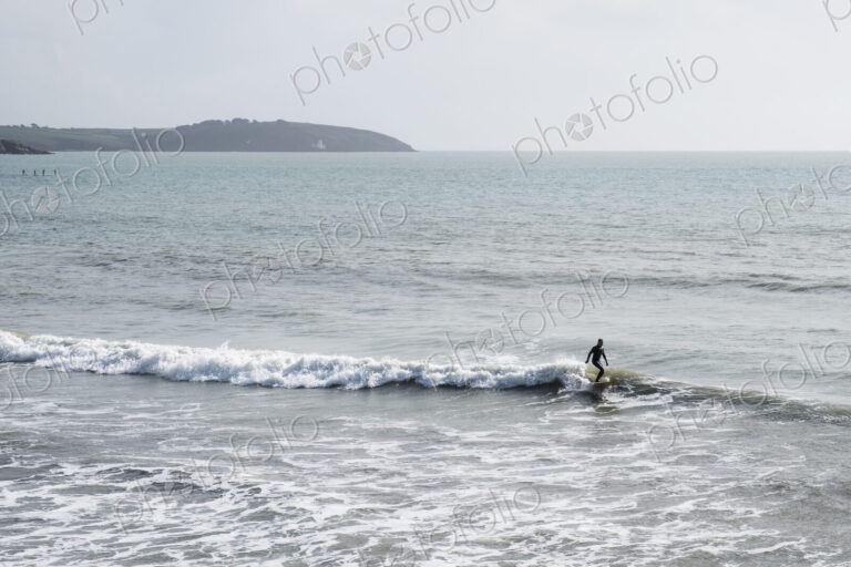 Surfer wearing wet suit riding ocean wave close to shore. need model release form!
