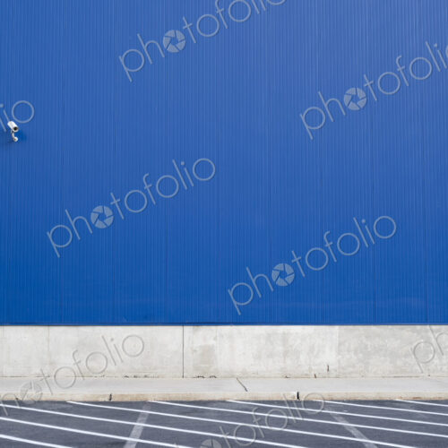 Surveillance camera on a blue exterior wall of warehouse or large windowless building.