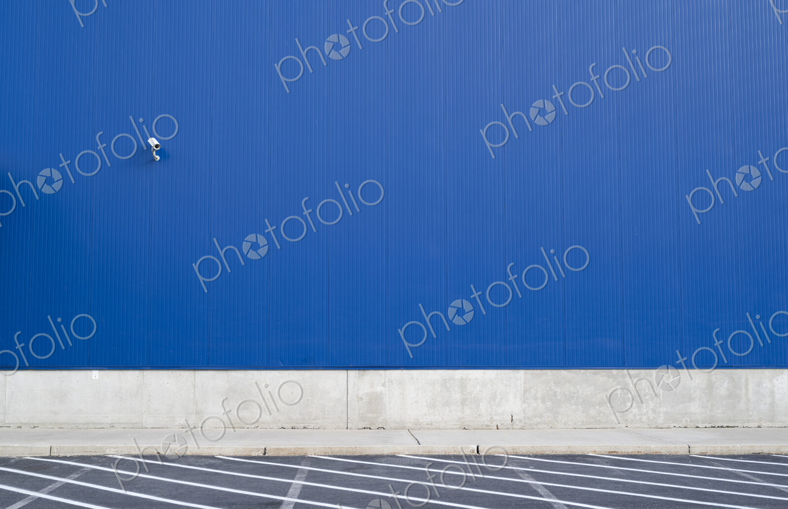 Surveillance camera on a blue exterior wall of warehouse or large windowless building.