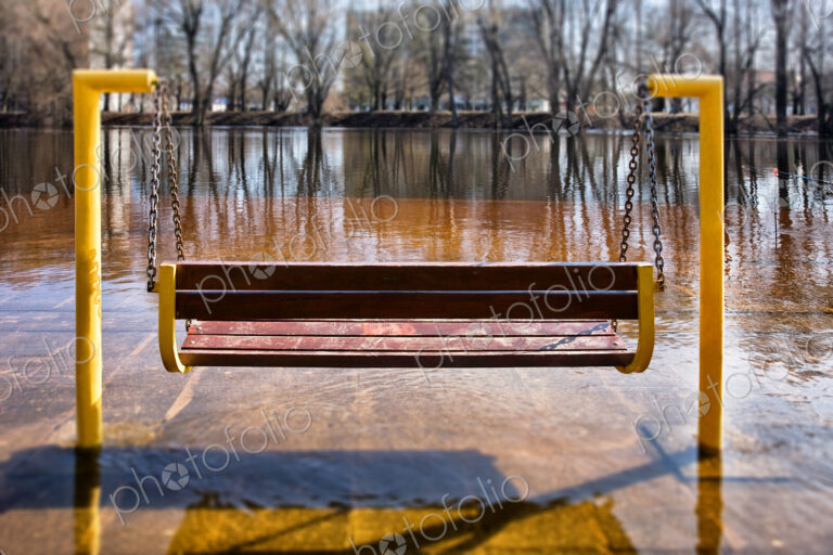 Swing seat in winter, a layer of ice covering paving and the surface of a lake.