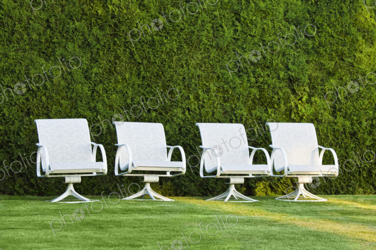 Swivel chairs in front of a hedge on grass.