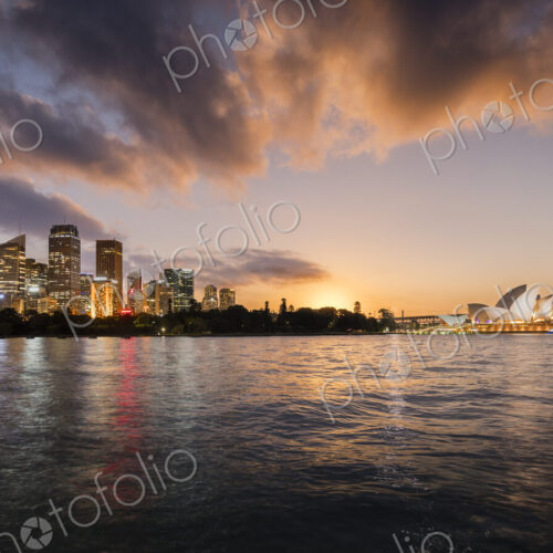 Sydney lit up at dawn seen from the water, including the Sydney Opera House.