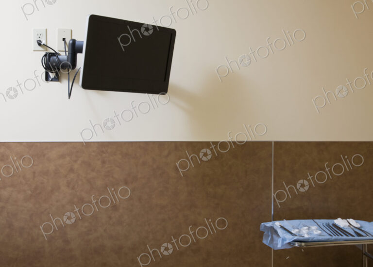 TV screen on wall of hospital with tray of surgical instruments on table.