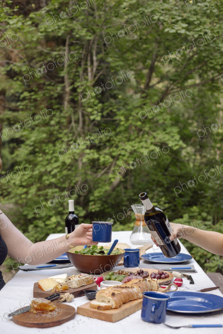 Table in a garden set with plates and food, a man pouring a glass of wine.