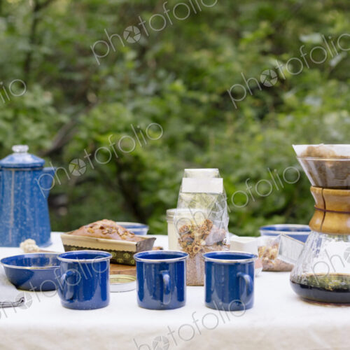 Table in a garden, with a coffee maker, mugs and bowls, a cake and cereal.