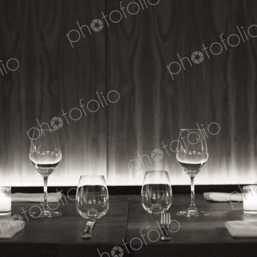 Table set with wine glasses, napkins and candles at a city restaurant. Black and white…