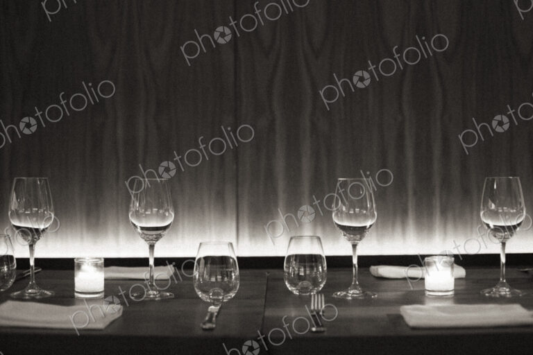 Table set with wine glasses, napkins and candles at a city restaurant. Black and white…