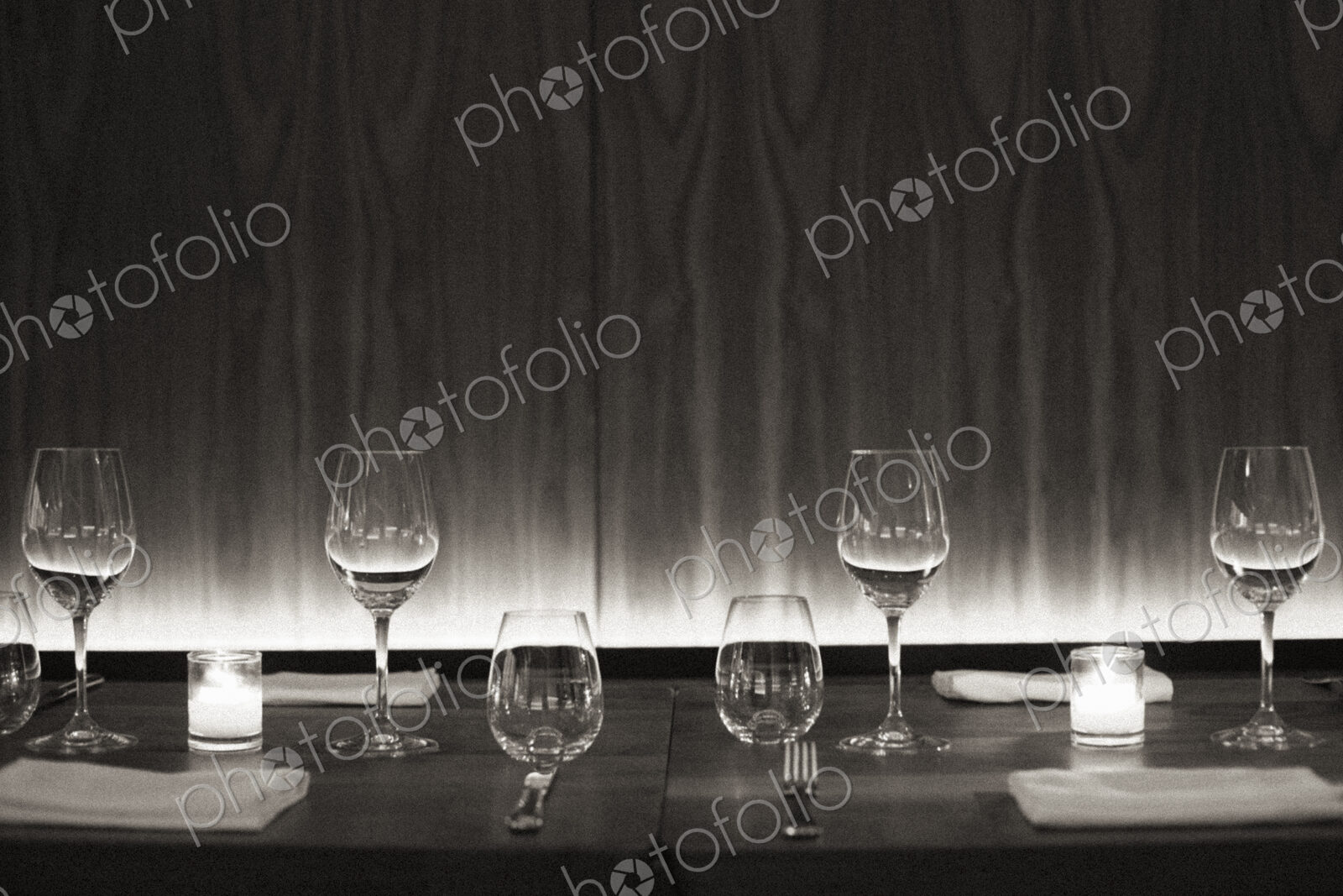 Table set with wine glasses, napkins and candles at a city restaurant. Black and white…