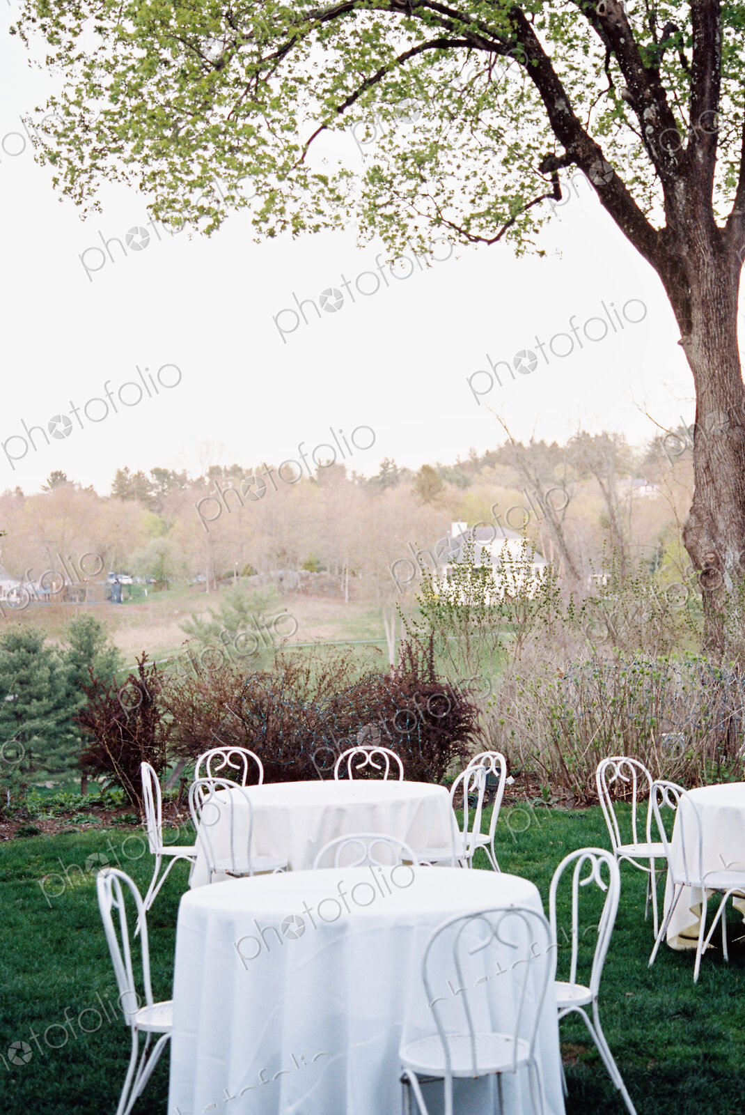 Tables and chairs set with white table clothes in a hotel garden overlooking a wooded…