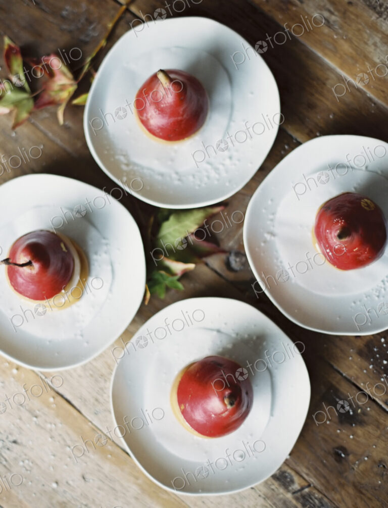 Tabletop viewed from above. Four plates with dessert. Pears dipped in sauce.