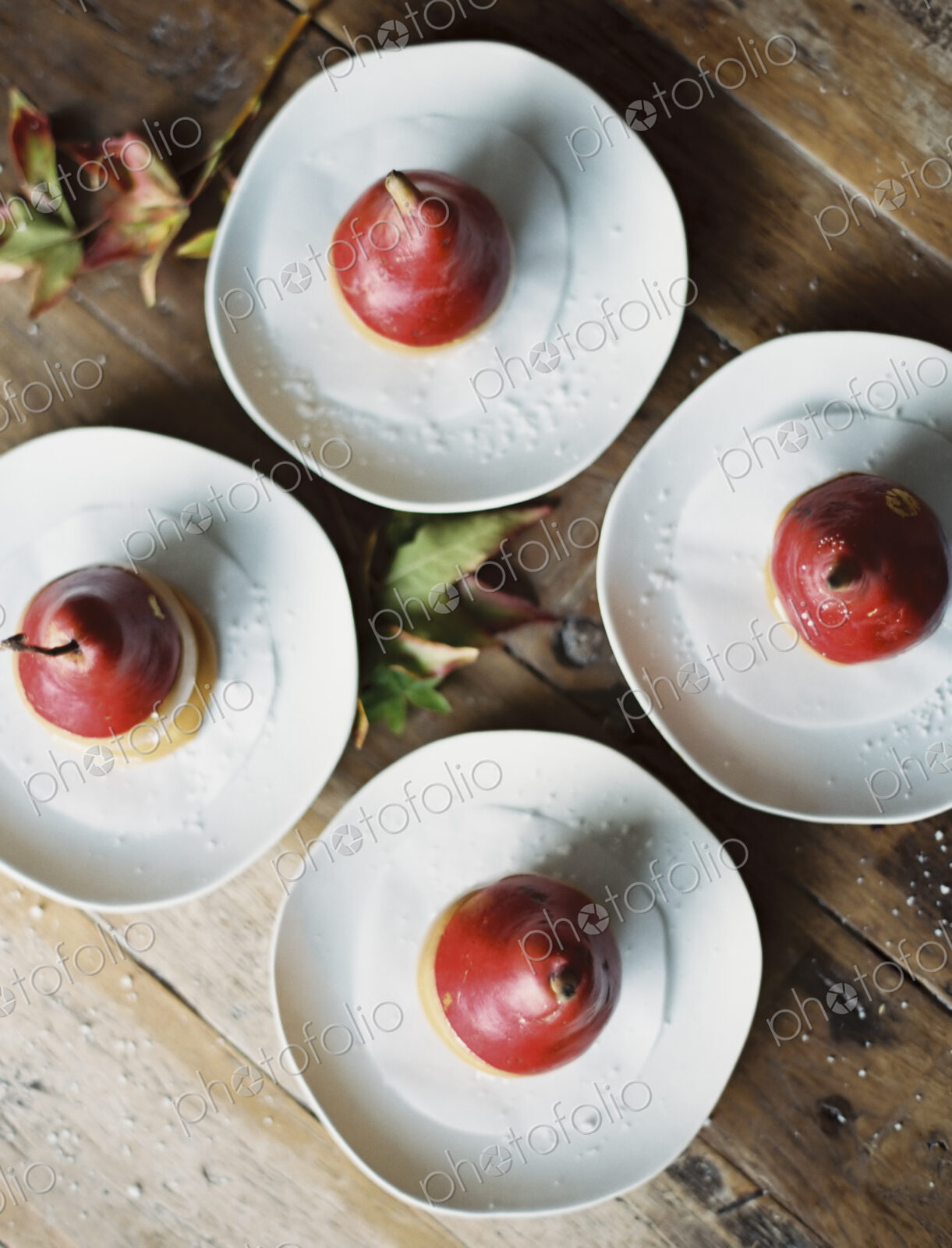 Tabletop viewed from above. Four plates with dessert. Pears dipped in sauce.