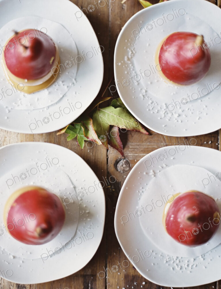 Tabletop viewed from above. Four plates with dessert. Pears dipped in sauce.