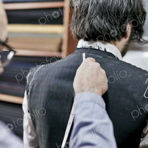 Tailor using measuring tape on a suit jacket, fitting the garment on a customer Tailor using measuring tape on a suit jacket, fitting the garment on a customer