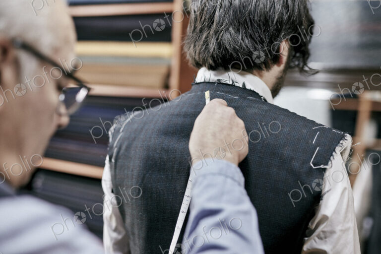 Tailor using measuring tape on a suit jacket, fitting the garment on a customer