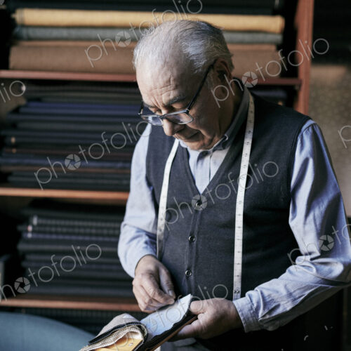Tailor with measuring tape around his neck inspecting fabric samples. Tailor with measuring tape around his neck inspecting fabric samples.