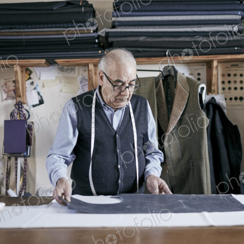 Tailor with measuring tape around neck working on a cut piece of fabric. Tailor with measuring tape around neck working on a cut piece of fabric.