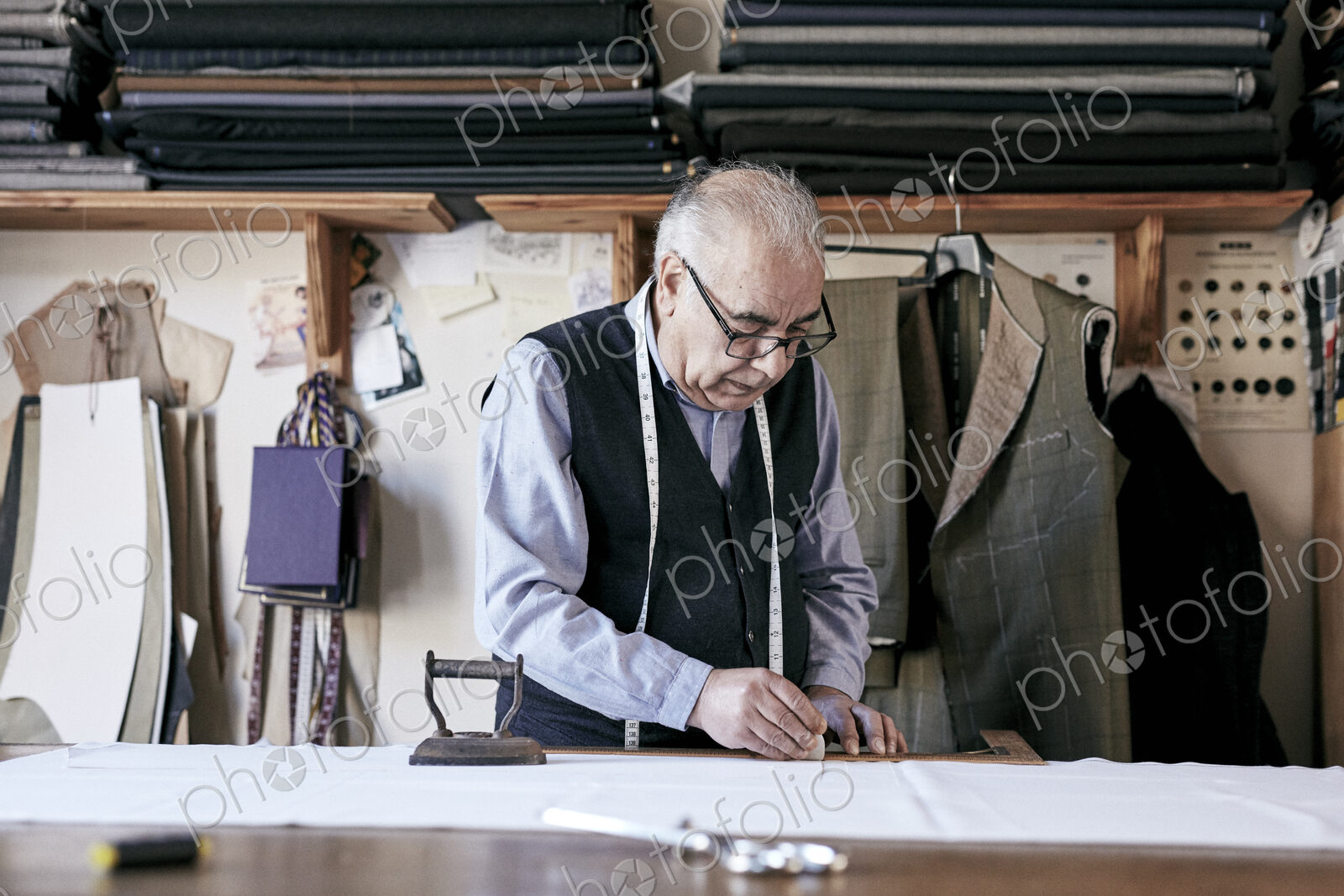 Tailor with measuring tape around neck working with material at bench