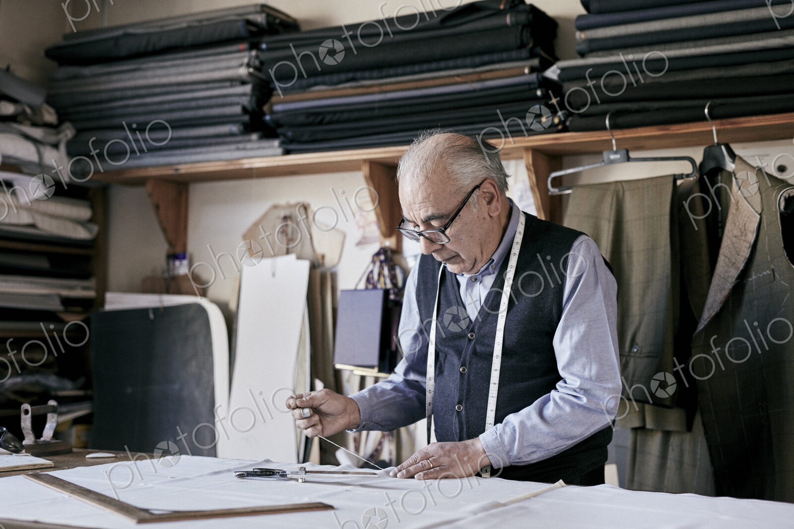 Tailor with measuring tape around neck working with material at bench