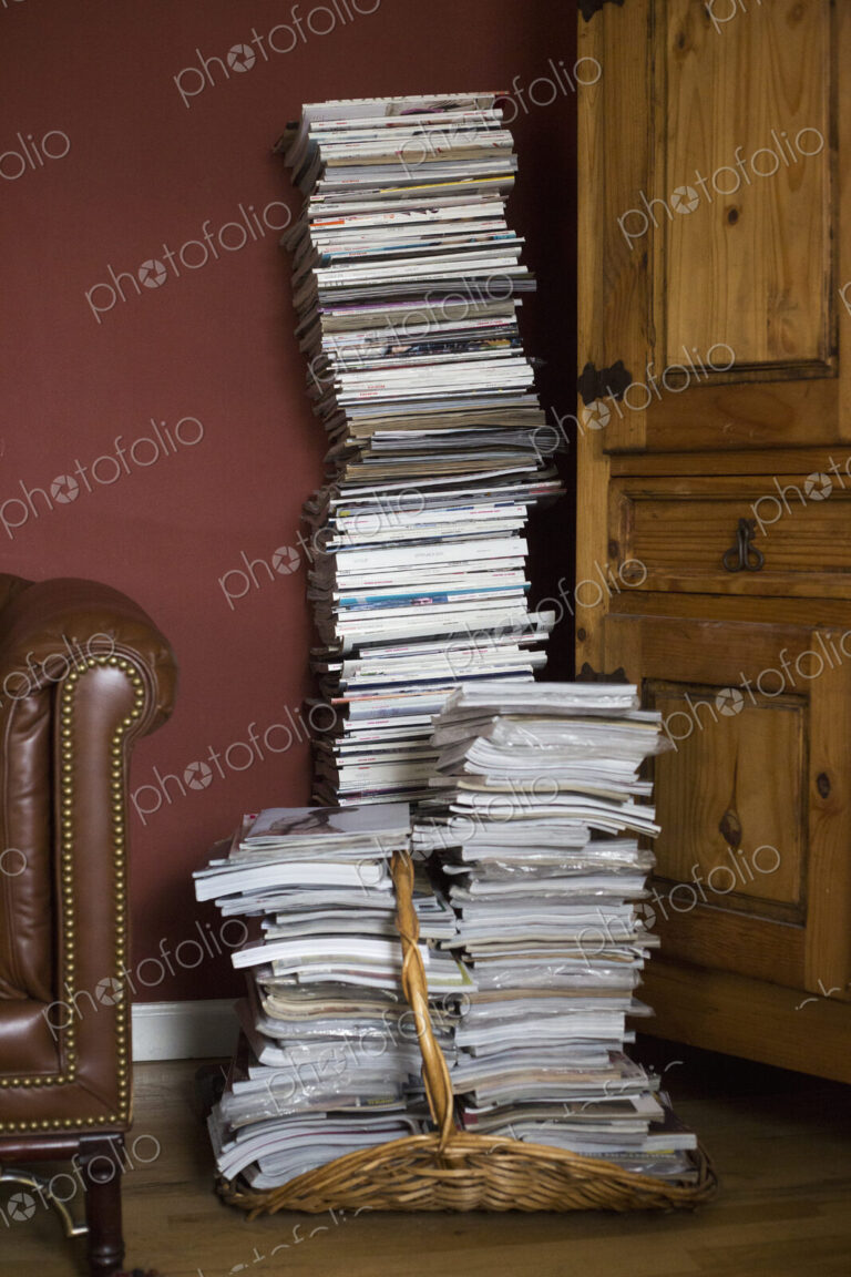 Tall stack of magazines in a basket leaning against a wall.