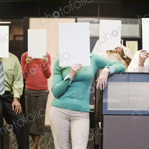 Team of business people standing with blank pieces of paper in front of their faces.