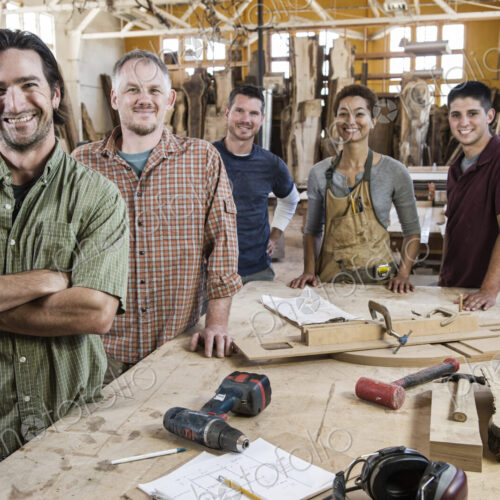 Team of multi-racial factory workers standing next to a work station in a large wood…