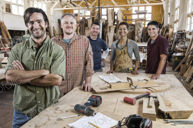 Team of multi-racial factory workers standing next to a work station in a large wood…