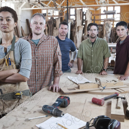 Team of multi-racial factory workers standing next to a work station in a large wood…