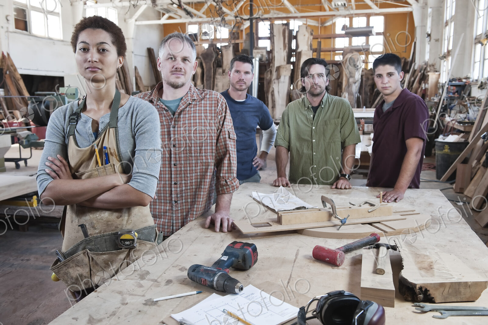 Team of multi-racial factory workers standing next to a work station in a large wood…