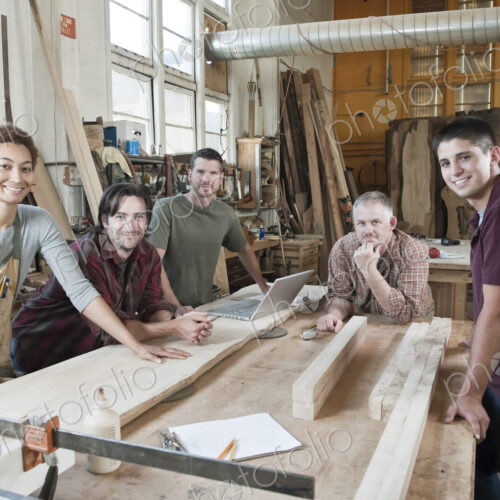 Team of multi-racial factory workers standing next to a work station in a large wood…