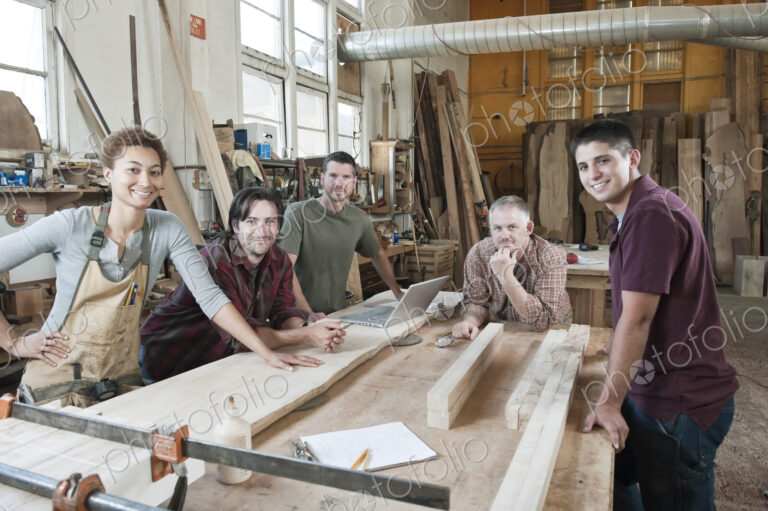 Team of multi-racial factory workers standing next to a work station in a large wood…