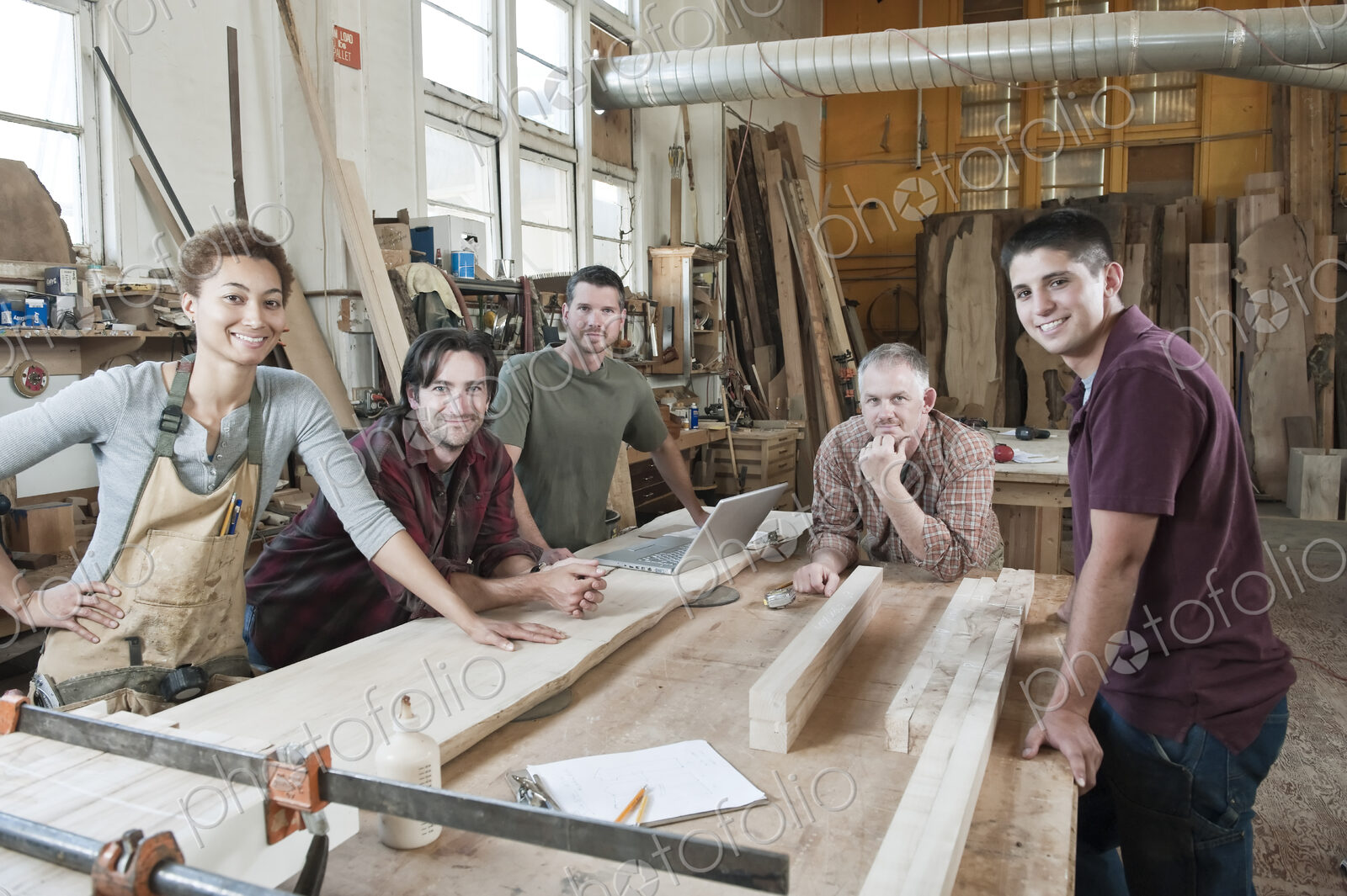 Team of multi-racial factory workers standing next to a work station in a large wood…