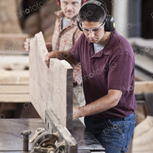 Team of two caucasian men cutting a large wooden slab on a table saw in a woodworking…