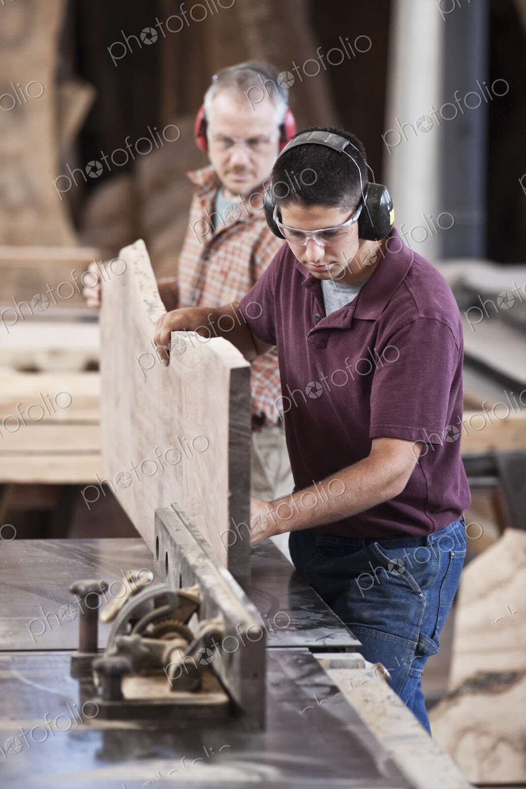 Team of two caucasian men cutting a large wooden slab on a table saw in a woodworking…