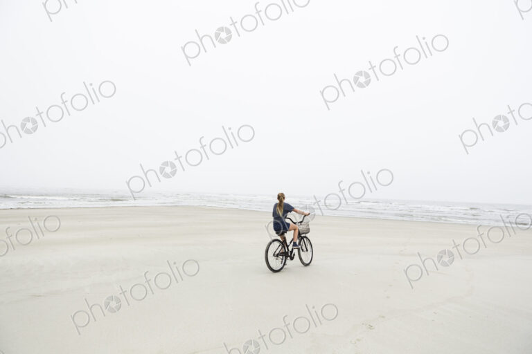 Teen girl biking on sandy beach by the ocean, St. Simon's Island, Georgia