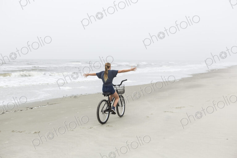 Teen girl biking on sandy beach by the ocean, St. Simon's Island, Georgia