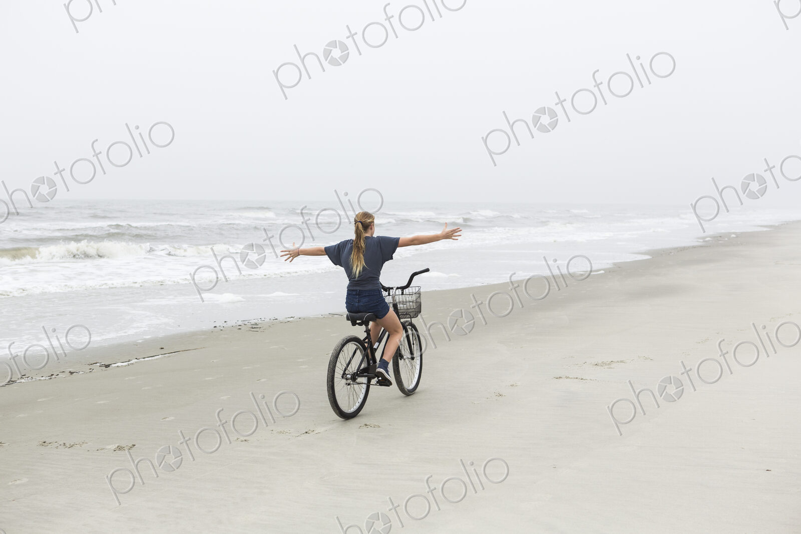 Teen girl biking on sandy beach by the ocean, St. Simon’s Island, Georgia